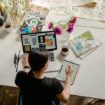 photo of woman writing on tablet computer while using laptop