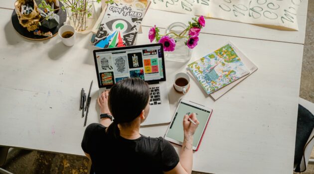 photo of woman writing on tablet computer while using laptop